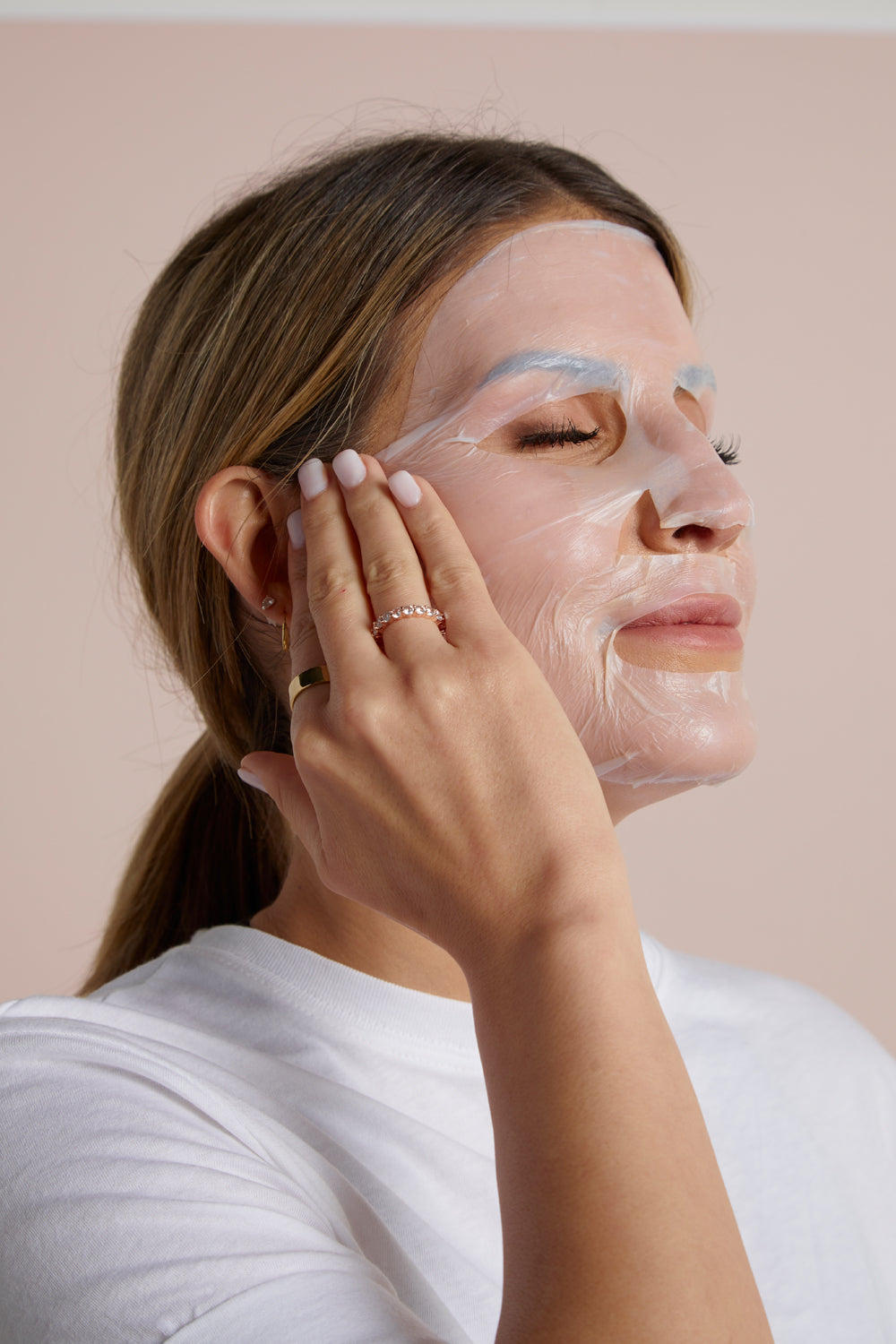 Woman applying a Winged Radiance facial sheet mask to her face